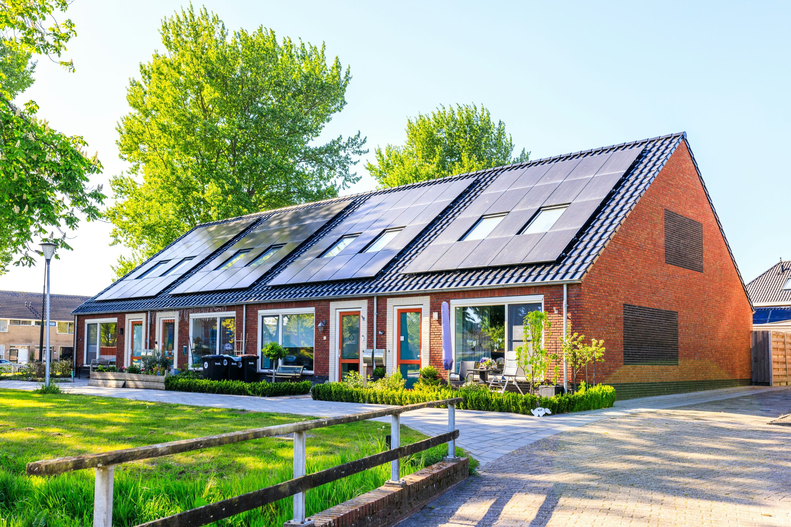 Nieuwbouwwoningen met zonnenpanelen in groene wijk. Tips om nieuwbouw koel te houden in de zomer